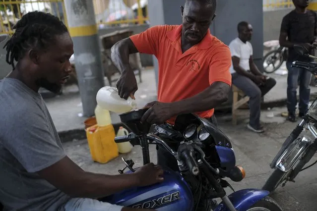 A man pours a small amount of gasoline into a motorcycle's fuel tank amid gas shortages during the general strike in Port-au-Prince, Haiti, Monday, October 18, 2021. (Photo by Matias Delacroix/AP Photo)