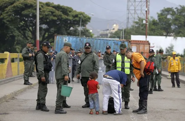 Venezuelan soldiers inspect a man's bag on the Simon Bolivar International Bridge, where cargo trailers block it, behind, seen from La Parada near Cucuta, Colombia, on the border with Venezuela, Sunday, April 14, 2019. Venezuelan authorities have limited the use of the bridge to students, seniors and the sick. U.S. Secretary of State Mike Pompeo is on a four-day Latin American tour, making his final stop at the Colombian border to meet with representatives of Venezuelan refugees. (Photo by Fernando Vergara/AP Photo)