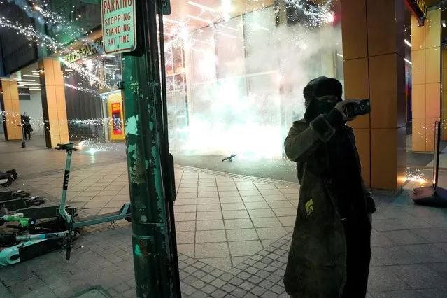 A person films as a firework explodes behind them during demonstrations related to the death of Manuel Teran who was killed during a police raid inside Weelaunee People's Park, the planned site of a controversial “Cop City” project, in Atlanta, Georgia, U.S., January 21, 2023. (Photo by Cheney Orr/Reuters)