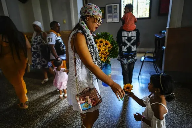 A mother and daughter prepare to make an offering of sunflowers to the Virgin of Charity of Cobre at her shrine in El Cobre, Cuba, Sunday, February 11, 2024. The Vatican-recognized Virgin, venerated by Catholics and followers of Afro-Cuban Santeria traditions, is at the heart of Cuban identity, uniting compatriots from the Communist-run Caribbean island to those who were exiled or emigrated to the U.S. (Photo by Ramon Espinosa/AP Photo)