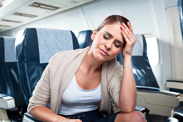 A young woman sitting on an airplane and suffering from headache. *Photo by izusek/Getty Images)