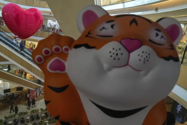 A cartoon tiger is displayed as shoppers wearing face masks to help protect fro the coronavirus ride on escalators at a mall during the Lunar New Year Eve in Beijing, Monday, January 31, 2022. The pandemic is muting Lunar New Year celebrations again this year, though people around Asia are finding ways to mark the traditional holiday despite restrictions on travel, restaurants and large gatherings. The Lunar New Year falls on Tuesday. (Photo by Andy Wong/AP Photo)