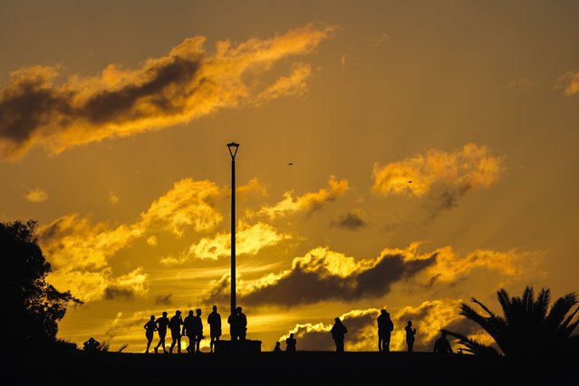 People gather at a headland as the sun rises at Coogee Beach in Sydney, Australia, Thursday, April 25, 2024. (Photo by Mark Baker/AP Photo)