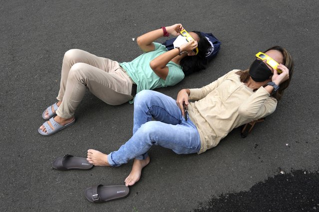 People lie on the ground as they use protective glasses to watch solar eclipse in Jakarta, Indonesia, Thursday, April 20, 2023. A rare solar eclipse will cross over remote parts of Australia, Indonesia and East Timor on Thursday. (Photo by Tatan Syuflana/AP Photo)