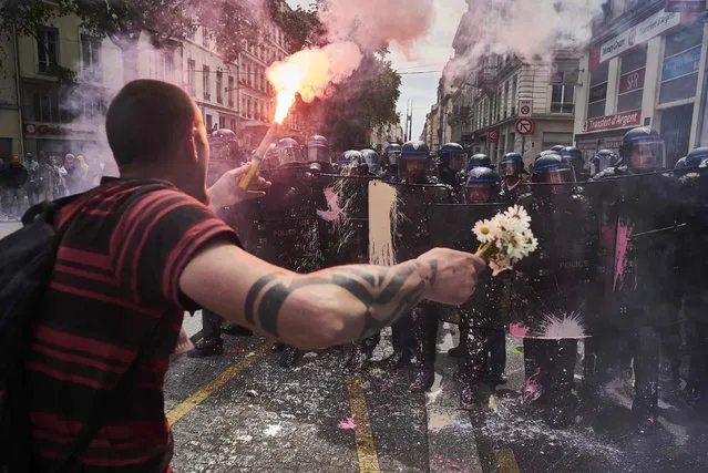 A man holds a bouquet of flowers and a torch as he faces riot police during a demonstration against the government's planned labour reform, on May 26, 2016 in Lyon, central eastern France. The French government's labour market proposals, which are designed to make it easier for companies to hire and fire, have sparked a series of nationwide protests and strikes over the past three months. (Photo by Jean-Philippe Ksiazek/AFP Photo)