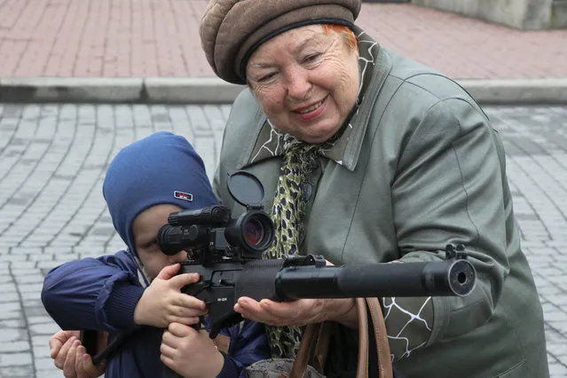 A woman assists a child, who points a weapon during an exhibition displaying military equipment, vehicles and weapons of the Russian defence artillery forces in the Black Sea port of Sevastopol, Crimea April 12, 2019. (Photo by Alexey Pavlishak/Reuters)