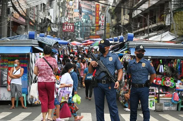 A policeman carrying an automatic rifle stands guard with a colleague along a popular market street in Manila on June 1, 2022, as security forces are on heightened alert in the capital following the twin bombings in Basilan island, near Jolo, a stronghold of Muslim militants. (Photo by Ted Aljibe/AFP Photo)
