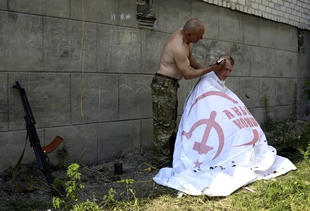 An Ukrainian serviceman from the Donbass volunteer battalion is covered with a Ukrainian Communist Party flag as he gets a hair cut on August 4, 2014 in eastern Ukrainian city of Popasna, Lugansk region, freed by Ukrainian forces from pro-Russian militants. (Photo by Anatolii Stepanov/AFP Photo)