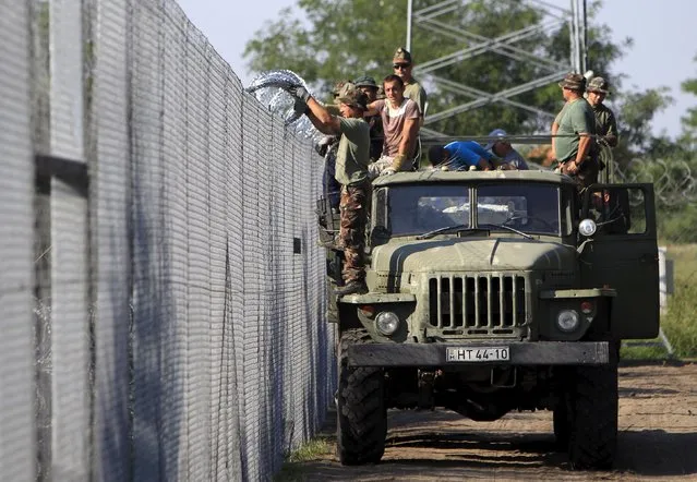 Hungarian soldiers adjust the razor wire on a fence near the town of Asotthalom, Hungary, August 30, 2015. About 100,000 migrants, many of them from Syria and other conflict zones in the Middle East, have taken the Balkan route into Europe this year, heading via Serbia for Hungary and Europe's Schengen zone of passport-free travel. (Photo by Bernadett Szabo/Reuters)