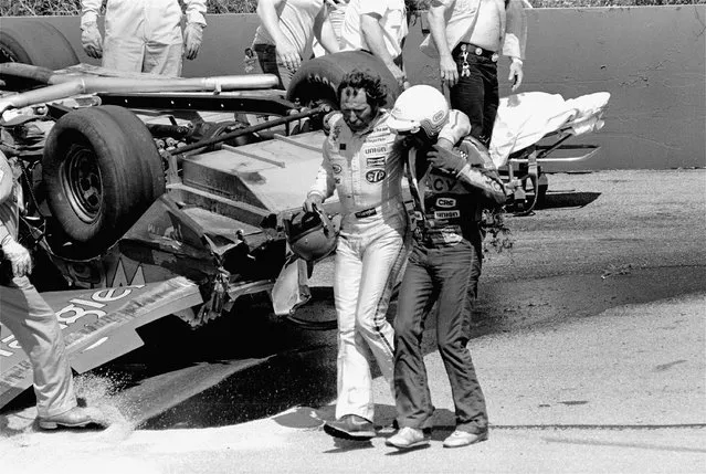 Tim Richmond of Charlotte, NC assists racing driver Dale Earnhardt of Mooresville, NC walking past Earnhardt's racing car overturned following an accident with the two drivers on the first turn of Pocono 500 NASCAR race at Pocono International Raceway in Long Pond, Pa. on Sunday July 25, 1982. Earnhardt injured his leg in the accident. (Photo by Rusty Kennedy/AP Photo)