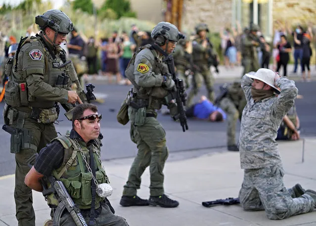 Albuquerque police detain members of the New Mexico Civil Guard, an armed civilian group, following the shooting of a man during a protest over a statue of Spanish conquerer Juan de Oñate on Monday, June 15, 2020, in Albuquerque, N.M. A confrontation erupted between protesters and a group of armed men who were trying to protect the statue before protesters wrapped a chain around it and began tugging on it while chanting: “Tear it down.” One protester repeatedly swung a pickax at the base of the statue. Moments later a few gunshots could be heard down the street and people started yelling that someone had been shot. (Photo by Adolphe Pierre-Louis/The Albuquerque Journal via AP Photo)
