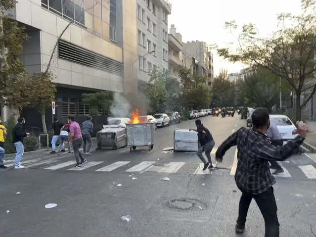 In this Tuesday, September 20, 2022, photo taken by an individual not employed by the Associated Press and obtained by the AP outside Iran, protesters throw stones at anti-riot police during a protest over the death of a young woman who had been detained for violating the country's conservative dress code, in downtown Tehran, Iran. Iran faced international criticism on Tuesday over the death of a woman held by its morality police, which ignited three days of protests, including clashes with security forces in the capital and other unrest that claimed at least three lives. (Photo by AP Photo/Stringer)