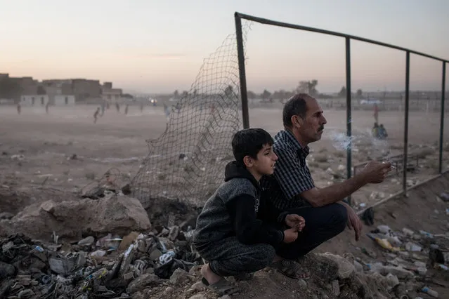 A father sits with his son to watch a local football game in East Mosul on November 5, 2017 in Mosul, Iraq. (Photo by Chris McGrath/Getty Images)