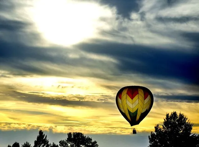 A hot air balloon floats over farm fields south of Washington, Ill., as the sun slips behind clouds on the autumn afternoon of Wednesday, September 24, 2014. (Photo by Ron Johnson/AP Photo/Peoria Journal Star)