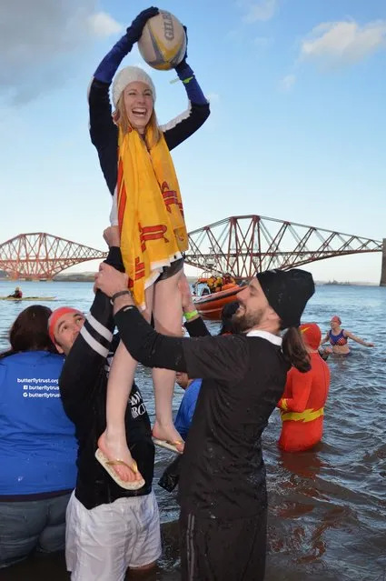 Two men lift a woman holding a rugby ball as they joined over 1,000 New Year swimmers, many in costume, braved freezing conditions in the River Forth in front of the Forth Rail Bridge during the annual Loony Dook Swim on January 1, 2013 in South Queensferry, Scotland. Thousands of people gathered last night to see in the New Year at Hogmanay celebrations in towns and cities across Scotland.  (Photo by Jeff J. Mitchell)