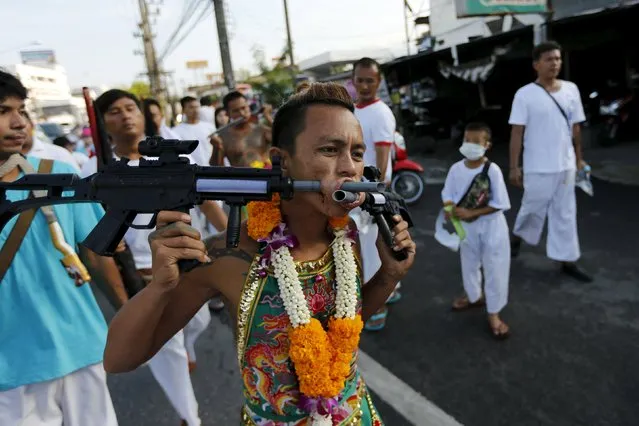 A devotee of the Chinese Ban Tha Rue shrine walks with guns pierced through his cheeks during a procession celebrating the annual vegetarian festival in Phuket, Thailand, October 17, 2015. (Photo by Jorge Silva/Reuters)