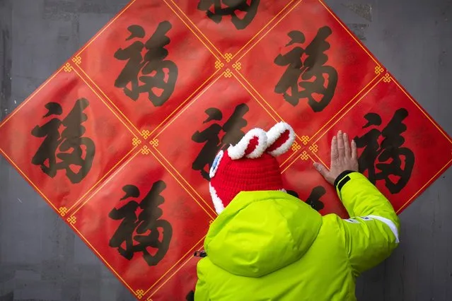 A woman uses her hand to smooth out decorations for the upcoming Lunar New Year that she put up on a wall at a tourist shopping street in Beijing, Saturday, January 21, 2023. The Year of the Rabbit officially begins on Sunday. (Photo by Mark Schiefelbein/AP Photo)