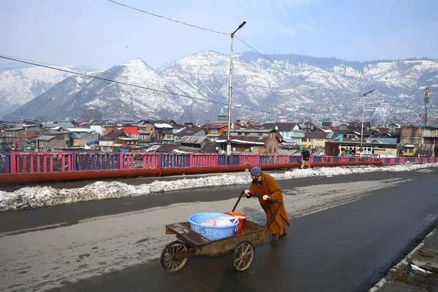 A man pushes a hand cart as snow covered mountains are seen in Baramulla Jammu and Kashmir India on 03 January 2023 (Photo by Nasir Kachroo/NurPhoto via Getty Images)