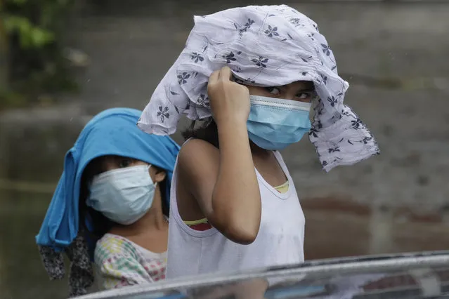 Young girls wearing masks to prevent the spread of the coronavirus place clothes to shelter them from rain due to Typhoon Molave in Pampanga province, northern Philippines on Monday, October 26, 2020. (Photo by Aaron Favila/AP Photo)