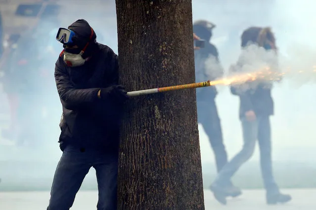 A protester stands behind a tree as he fires a roman candle during clashes French CRS riot police during a demonstration in Nantes, France, April 14, 2018. (Photo by Stephane Mahe/Reuters)