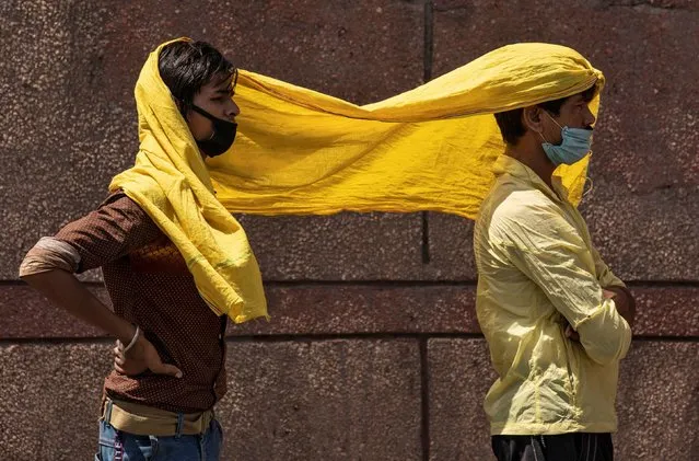 Migrant workers cover themselves with a scarf, to protect from heat as they wait to get registered before boarding a train to their home state of eastern Bihar, during an extended lockdown to slow the spreading of the coronavirus disease (COVID-19), in New Delhi, India, May 21, 2020. (Photo by Danish Siddiqui/Reuters)