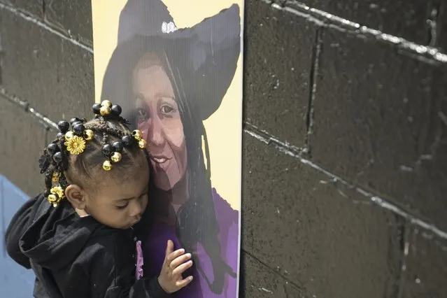 Naujaj Buchanan, 2, nestles close to a portrait of her godmother, shooting victim Geraldine Talley, across the street from Tops Friendly Market as victims of last year's mass shooting at the supermarket were remembered, in Buffalo, N.Y., Sunday, May 14, 2023. (Photo by Libby March/The Buffalo News via AP Photo)