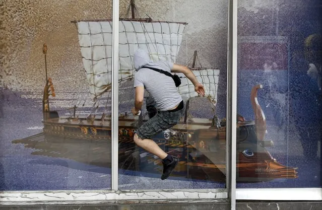 A demonstrator jumps to attempt to break a window displaying an image of an ancient greek galley during protests against austerity measures in Athens, in this June 28, 2011 file photo. (Photo by Yorgos Karahalis/Reuters)