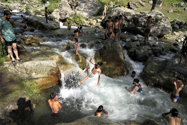 A Kashmiri boy jumps as he along with others cool off at a stream on a hot summer day on the outskirts of Srinagar, Indian controlled Kashmir, Tuesday, July 4, 2023. The Indian portion of Kashmir has been experiencing extremely hot weather this week. (Photo by Mukhtar Khan/AP Photo)