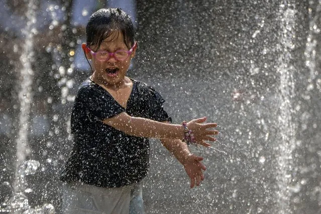 A girl reacts as she plays in a fountain at a shopping mall in Beijing, Friday, June 23, 2023. Authorities issued a rare red alert for high temperatures in parts of China's capital on Friday, the highest level of warning, as highs were expected to once again climb to around 40 degrees Celsius (104 degrees Farenheit). (Photo by Mark Schiefelbein/AP Photo)
