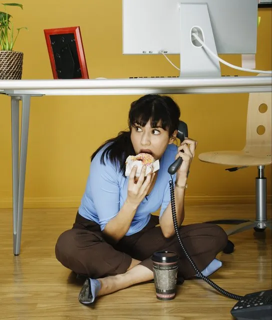 Businesswoman eating lunch under desk. (Photo by Hill Street Studios/Getty Images)