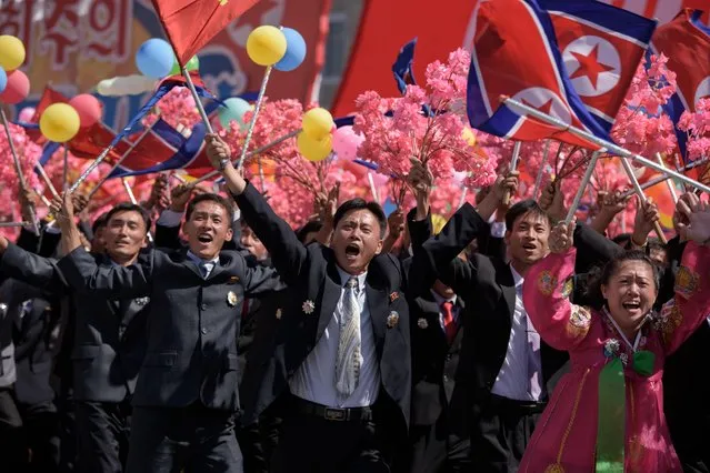 Participants wave flowers as they march past a balcony from where North Korea' s leader Kim Jong Un was watching, during a mass rally on Kim Il Sung square in Pyongyang on September 9, 2018. (Photo by Ed Jones/AFP Photo)