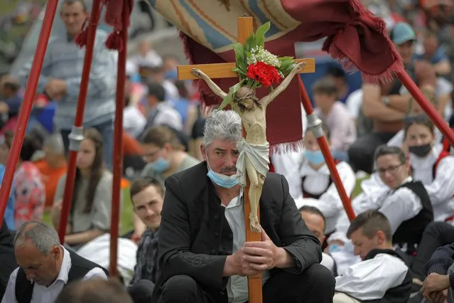 A man holds a crucifix as Catholic pilgrims fill the hillsides after tens of thousands joined their faith's biggest religious event in Sumuleu Ciuc, Romania, Saturday, May 22, 2021. More than 35,000 Catholic pilgrims congregated at an open-air shrine in Sumuleu Ciuc in Transylvania on Saturday for an age-old procession that last year was canceled due to the coronavirus pandemic. (Photo by Vadim Ghirda/AP Photo)
