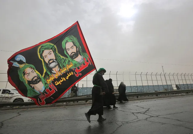 A Shiite Muslim pilgrim walks carrying a flag depicting the Prophet Mohammed's cousin Ali ibn Abi Taleb (C) and his two sons Hussein (R) and Abbas (L), on the outskirts of the Iraqi capital Baghdad on the way towards the central holy Iraqi city of Karbala on October 26, 2018, ahead of the Arbaeen religious festival which marks the 40th day after Ashura, commemorating the seventh century killing of the revered Imam Hussein. (Photo by Ahmad Al-Rubaye/AFP Photo)