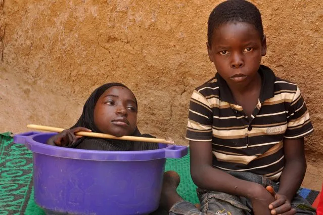Rahma, 19, pictured with her 10-year old brother Fahad on June 21, 2016 in Kano, Nigeria. A teenage girl born without limbs lives her life in a plastic bowl. Rahma Haruna is a bright, happy girl, despite suffering from a mystery condition that stopped her arms and legs developing properly – leaving her practically limbless and in constant pain. The 19-year- old, from Kano, Nigeria, was born a healthy baby but when she turned six months old her growth came to a sudden halt and she stopped hitting key development milestones. Rahma’s family do their best to provide her with a fulfilling life and transport her around the village in a plastic bowl. Rahma said: “They help me a lot. How do they? They give me anything I need”. Rahma died on 25 December 2016. (Photo by Sani Maikatanga/Barcroft Images)