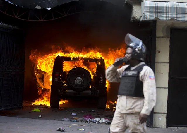A police officer stands in front of a burning car set alight by protesters during a protest to demand the resignation of President Jovenel Moise and demanding to know how Petro Caribe funds have been used by the current and past administrations, in Port-au-Prince, Haiti, Thursday, February 7, 2019. (Photo by Dieu Nalio Chery/AP Photo)