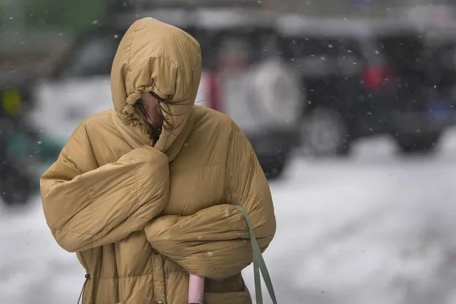A woman uses her winter clothes to shield from the wind and snow on a street as the capital is hit by snowstorm in Beijing, Sunday, November 7, 2021. An early-season snowstorm has blanketed much of northern China including the capital Beijing, prompting road closures and flight cancellations. (Photo by Andy Wong/AP Photo)