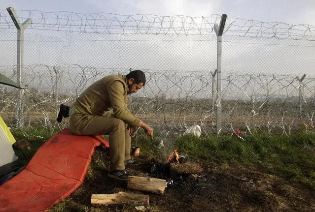 A refugee sits near a bonfire next to the border fence at the Greek-Macedonian border, in a makeshift camp near the village of Idomeni, Greece, March 23, 2016. (Photo by Alexandros Avramidis/Reuters)