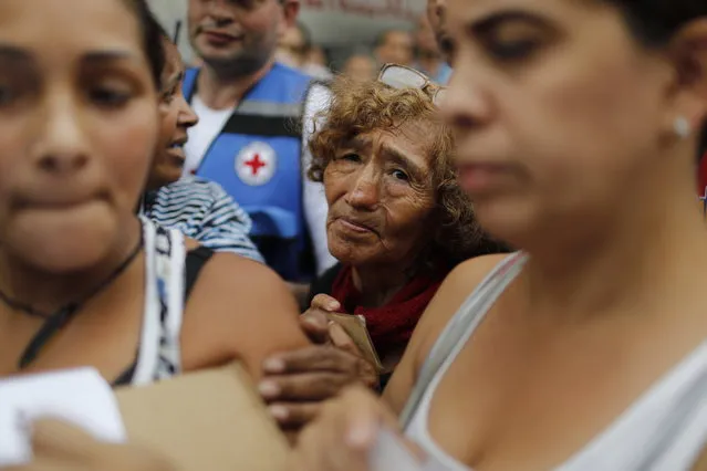 In this April 16, 2019 photo, people wait to be given empty water containers and water purification pills during the first aid shipment from the Red Cross in Caracas, Venezuela. In late March, the Red Cross federation announced it would soon begin delivering assistance to an estimated 650,000 people and vowed that it would not accept interference from either side of the polarized country. (Photo by Ariana Cubillos/AP Photo)