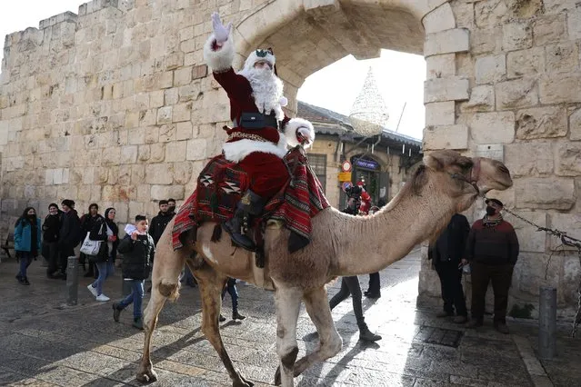 Issa Kassissieh, dressed as Santa Claus, rides a camel near the Jaffa Gate in Old City of Jerusalem, 23 December 2021, ahead of the Christ​mas Holiday. (Photo by Abir Sultan/EPA/EFE)