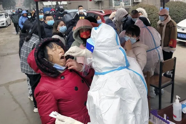A medical worker wearing a protective suit takes swab samples for the COVID-19 test on residents in Huaxian county in central China's Henan province on Monday, January 10, 2022. A third Chinese city has locked down its residents because of a COVID-19 outbreak, raising the number confined to their homes in China to about 20 million people. (Photo by Chinatopix via AP Photo)