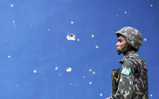 A Brazilian Army soldier walks past bullet holes in a wall during an operation in the Mare slums complex in Rio de Janeiro March 26, 2014. (Photo by Ricardo Moraes/Reuters)