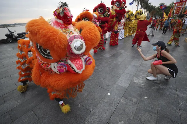 A tourist, right, takes a photo of Cambodian Chinese community people performing lion dance on Monday, January 31, 2022, ahead of Lunar New Year in Phnom Penh, Cambodia. (Photo by Heng Sinith/AP Photo)