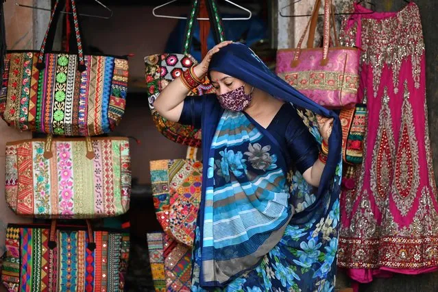 A woman shopkeeper adjusts her saree to cover her head while waiting for customers at a roadside shop in New Delhi on March 8, 2022, on the occasion of International Women's Day. (Photo by Sajjad Hussain/AFP Photo)