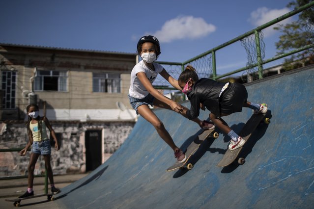 Eleven-year-old Yasmim Ferreira, facing camera, holds hands with eight-year-old Ana Julia dos Santos, during a skateboard class from the NGO “CDD Skate Arte”, at a public skate park in the City of God favela of Rio de Janeiro, Brazil, Thursday,  August 5, 2021. (Photo by Bruna Prado/AP Photo)