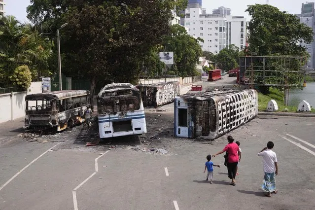 A Sri Lankan family watches the wreckage of buses burnt in clashes in Colombo, Sri Lanka, Wednesday, May 11, 2022. (Photo by Eranga Jayawardena/AP Photo)