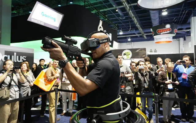 A man wearing an Oculus VR headset demonstrates a first person shooter game in a Virtuix Omni virtual reality system at the International Consumer Electronics show (CES) in Las Vegas, Nevada, January 6, 2015. Wearing special shoes with sensors, the player can actually run in the game. (Photo by Rick Wilking/Reuters)