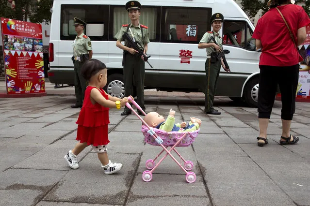 A child pushes a toy pram and doll past Chinese paramilitary on duty along a shopping street in Beijing, China, Friday, July 15, 2016. (Photo by Ng Han Guan/AP Photo)
