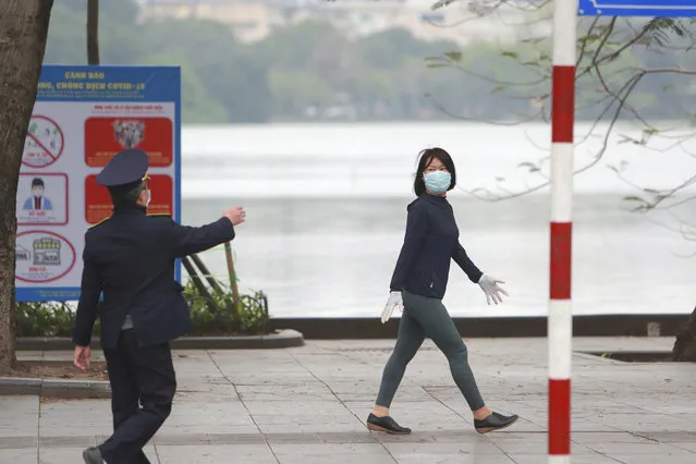 A security officer talks to a woman walking on a street in Hanoi, Vietnam, Wednesday, April 1, 2020. Vietnam on Wednesday starts two weeks of social distancing to contain the spread of COVID-19. (Photo by Hau Dinh/AP Photo)