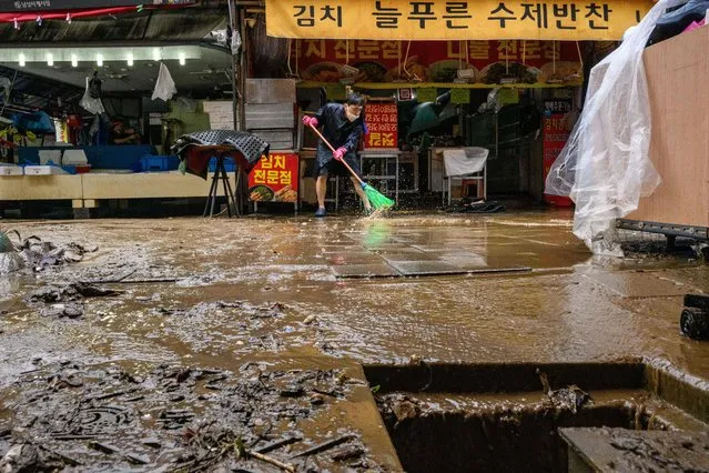 A worker sweeps away water at the historic Namseong Market in the Gangnam district of Seoul on August 9, 2022, after record-breaking rains caused severe flooding, with at least seven people dead and seven more missing, officials said. (Photo by Anthony Wallace/AFP Photo)