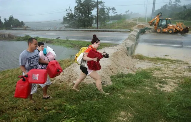 Residents carry pillows, blankets and fuel containers past a flood berm while evacuating an area of rising waters in Slidell, La., on Thursday, Aug. 30. (Photo by John Moore)